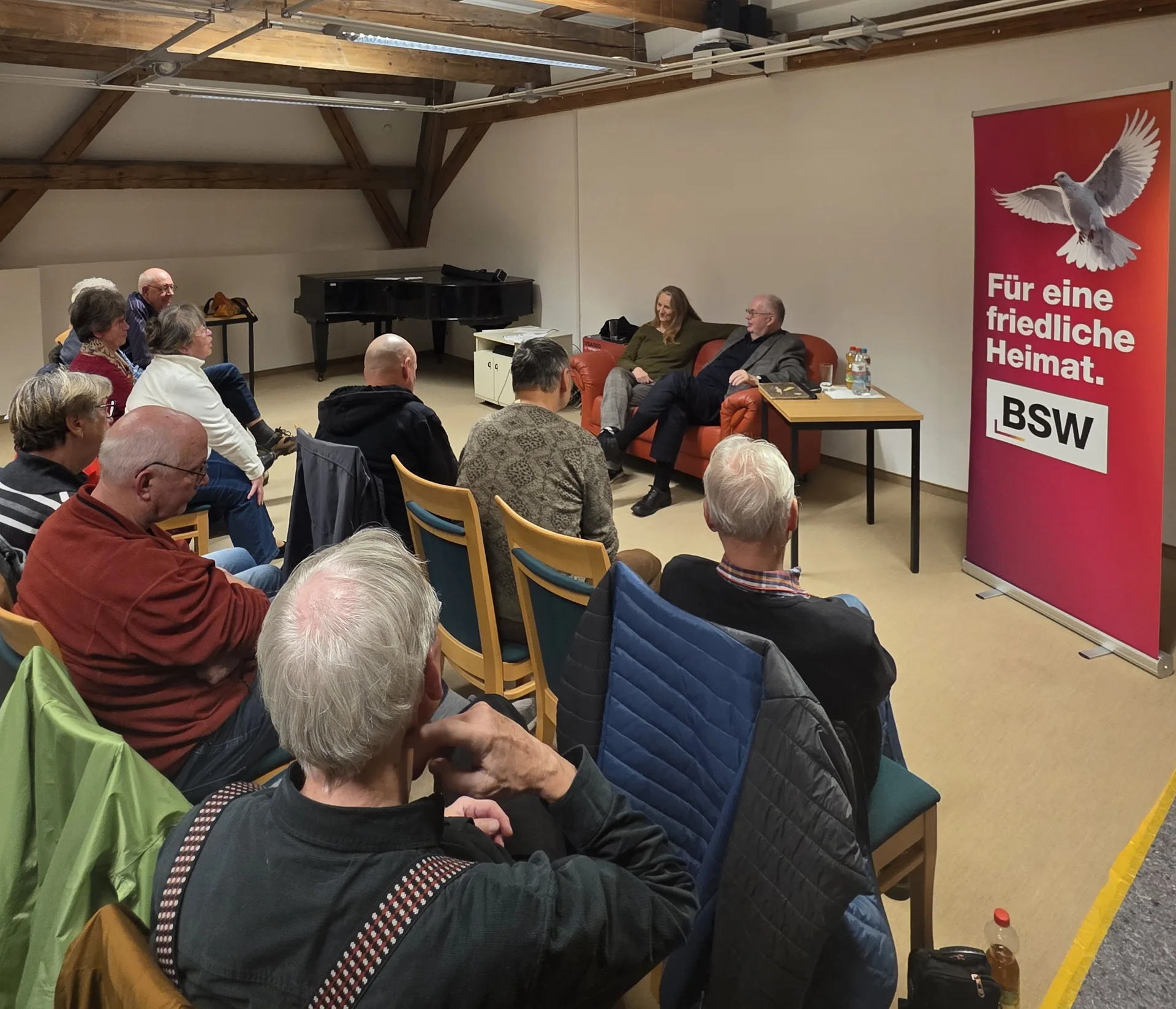 Publikum bei der Lesung in der Christian-Weise-Bibliothek Zittau; vorne sitzen zwei Vortragende auf einem roten Sofa, rechts steht ein BSW-Aufsteller.
