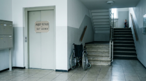 Stillgelegter Aufzug in einem älteren Wohnblock mit Treppenhaus und Rollstuhl als Symbol für fehlende Barrierefreiheit und die Isolation eines Rollstuhlfahrers in Olbersdorf.
